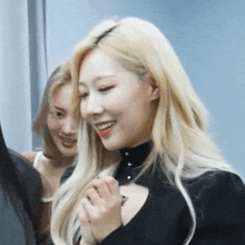 a woman with blonde hair is smiling while standing next to another woman with blonde hair .