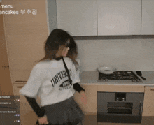 a woman in a white shirt with the word univers on it is dancing in a kitchen