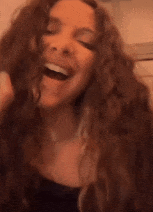 a woman with long curly hair is laughing with her mouth wide open