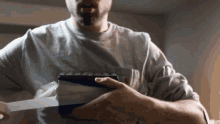 a man in a grey shirt is holding a blue and white object in his hands