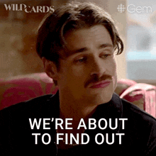 a man with a mustache is sitting on a couch and says " we 're about to find out "