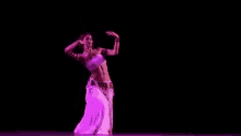 a woman in a white top and purple skirt is dancing on a stage in a dark room .