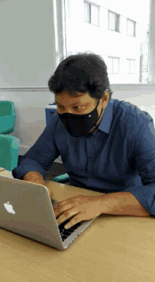 a man wearing a mask is typing on a laptop