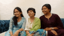 three women are posing for a picture while sitting on a blue couch