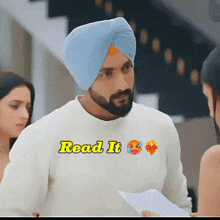 a man wearing a turban is holding a piece of paper with the words read it on his shirt