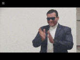 a man wearing sunglasses and a suit applauds