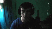 a man wearing headphones and glasses looks at the camera in a dark room .