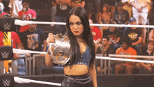 a woman in a wrestling ring is holding a championship trophy