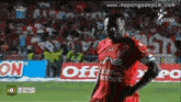 a soccer player in a red jersey stands on a field in front of a crowd