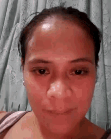 a close up of a woman 's face with a sweaty forehead and a curtain in the background .