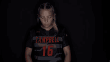 a girl wearing a campbell jersey stands in the dark