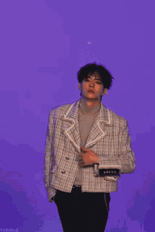 a young man is standing in front of a purple background and his jacket is open
