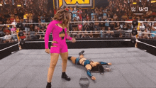 a woman in a pink outfit is standing next to a woman laying on the floor in a wrestling ring