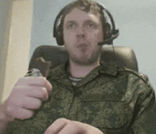 a man in a military uniform is eating a candy bar while wearing headphones .