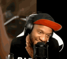 a man wearing headphones and a red hat is smiling in front of a microphone .