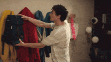 a man in a white shirt is reaching for a backpack hanging on a wall