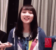 a woman wearing a blue hoodie and a rainbow shirt is smiling and making a funny face .