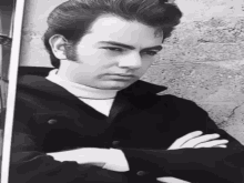 a man with his arms crossed is wearing a black jacket and white turtleneck