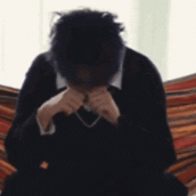 a man covering his face with his hands while sitting on a chair