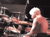 a shirtless man is playing drums in front of a microphone with the website koadmemoabilia.com in the corner