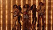 four women are dancing in front of a wall with lights on it