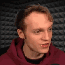 a young man wearing a red hoodie is looking at the camera .