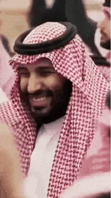 a man in a keffiyeh is smiling while standing in a crowd of people .