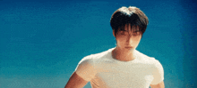 a young man wearing a white t-shirt is standing in front of a blue sky .