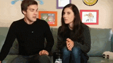 a man and a woman are sitting on a couch with a picture on the wall that says selfie on it