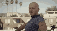 a bald man with a tattoo on his arm is holding a gun in front of a building .