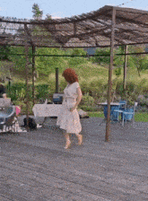 a woman in a white dress is standing on a wooden deck