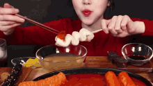 a woman in a red sweater is eating food with chopsticks .