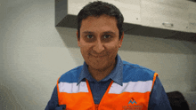 a man wearing a blue and orange vest with the letters m on the front