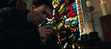 a man covering his face in front of a colorful stained glass window