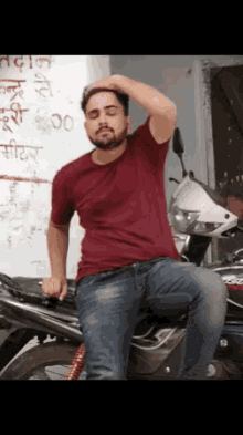 a man in a red shirt sits on a motorcycle with his hand on his head