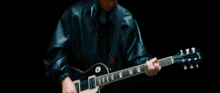 a man in a leather jacket is playing an electric guitar