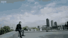 a man sits on the edge of a building with bbc written on the bottom right