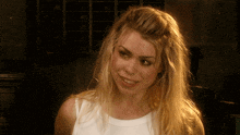 a blonde woman wearing a white tank top smiles