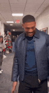 a man wearing a blue leather jacket is standing in a hallway .