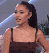 a woman with a ponytail is wearing a brown tank top and earrings