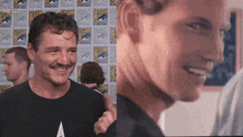 a man is smiling in front of a wall with comic con written on it