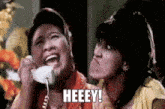 two women are talking on a telephone and one of them is saying heeey !