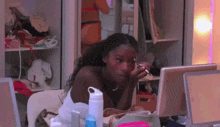 a woman is sitting in front of a laptop computer applying makeup .