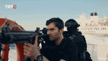 a man holding a gun in front of a ship that says guvenlik