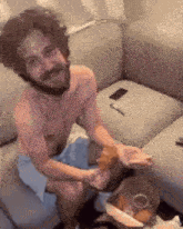 a shirtless man is sitting on a couch eating a pizza .