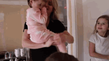 a woman is holding a baby in her arms while another girl looks on .