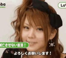 a woman wearing a headband with a bow and skull earrings is smiling