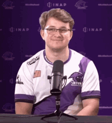 a man in a purple and white shirt is sitting in front of a microphone and smiling .