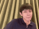 a young man is making a funny face in front of a curtain .