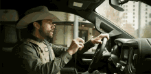 a man in a cowboy hat and vest is driving a car